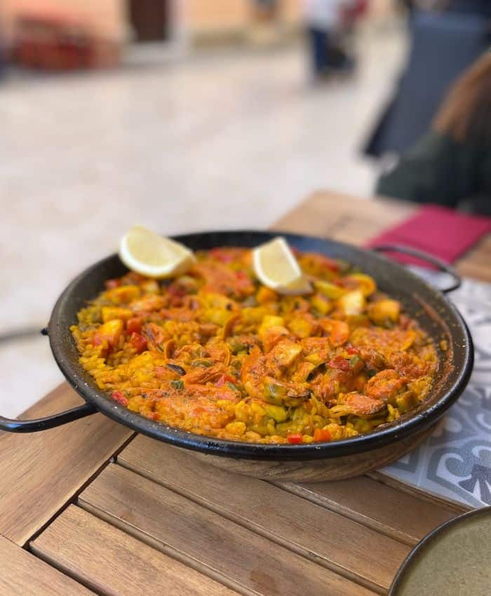 Close-up of a traditional Spanish paella with shrimp, lemon wedges, and vegetables, served in a shallow pan on a wooden table