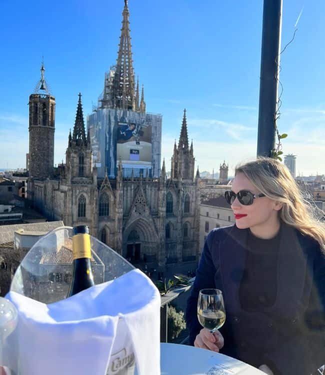 Girl with a glass of champagne sitting on a rooftop with a view of a cathedral in the background in Barcelona in March